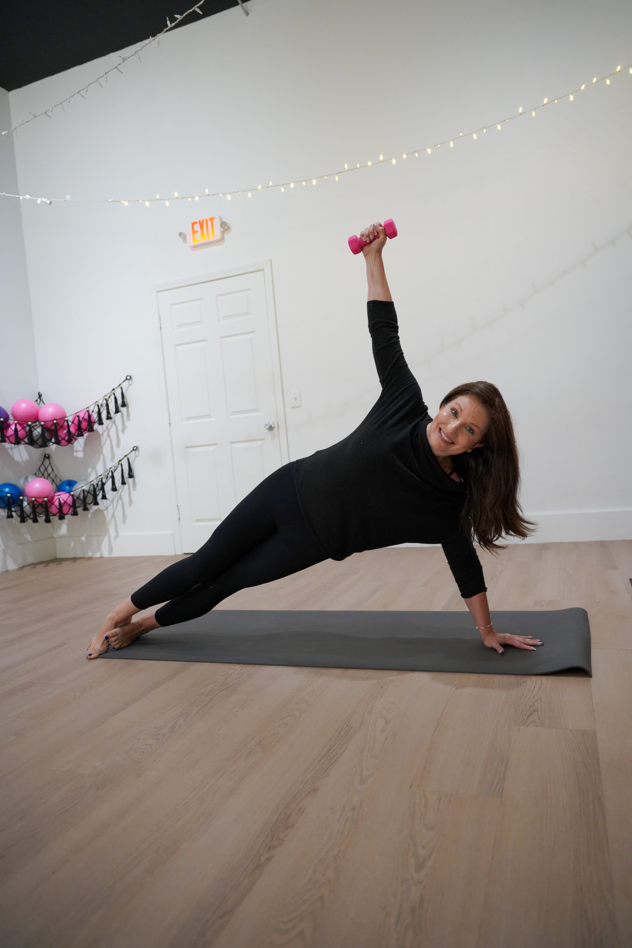 An instructor holding a side plank with a hand weight reaching overhead