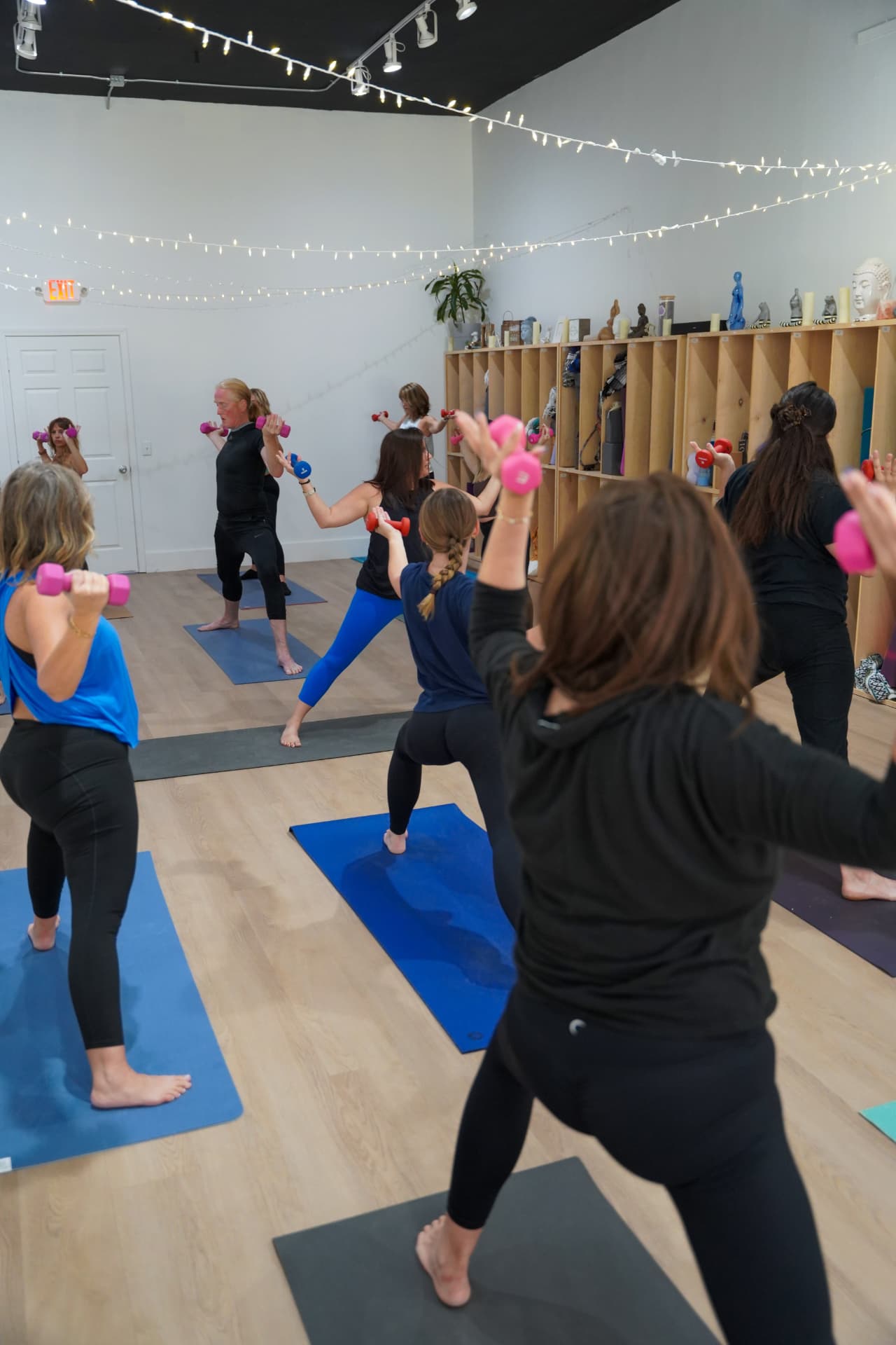 A student rowing hand weights in a warrior stance during yoga sculpt